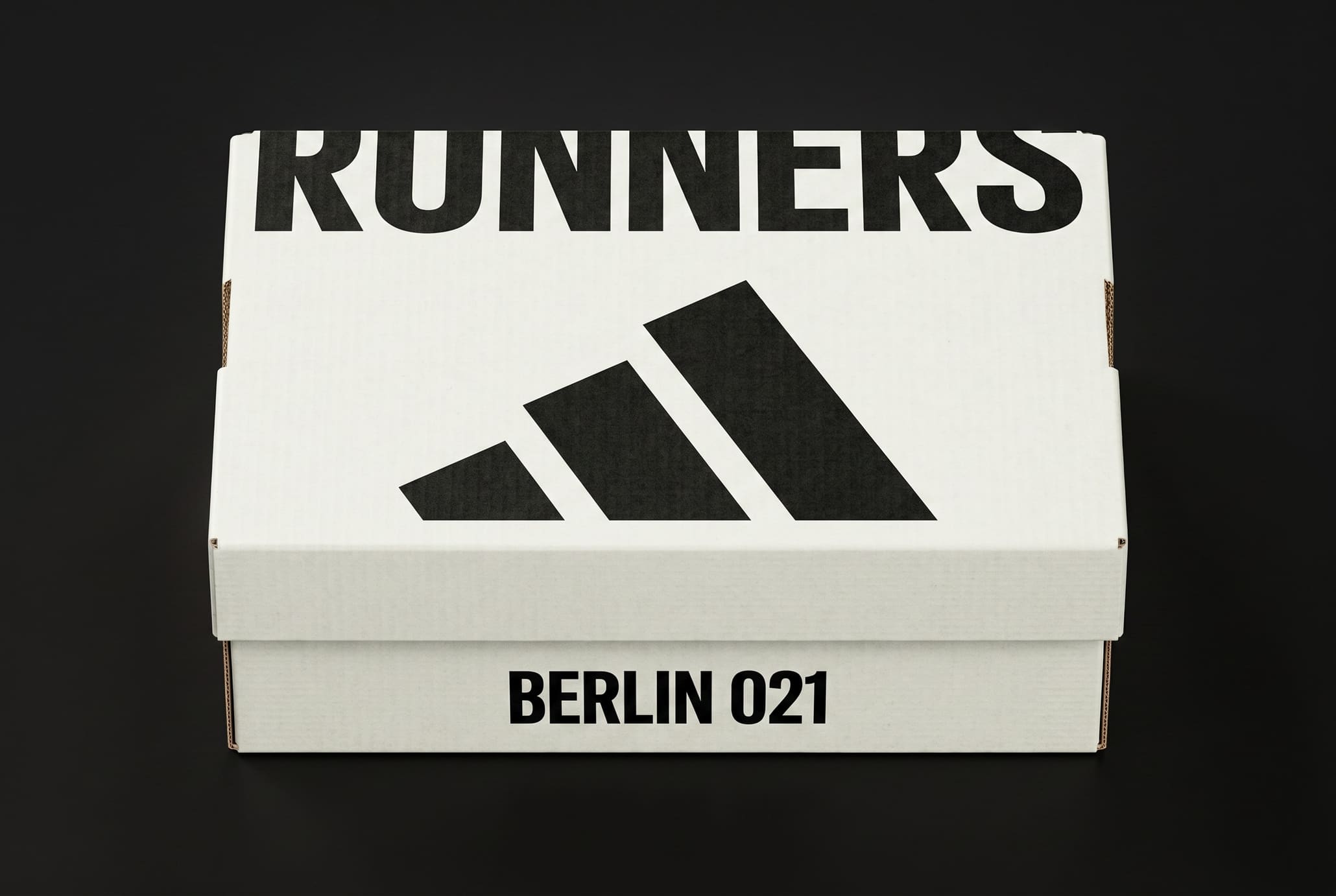White corrugated shoebox photographed on black, RUNNERS and three raked black bars printed across the lid
