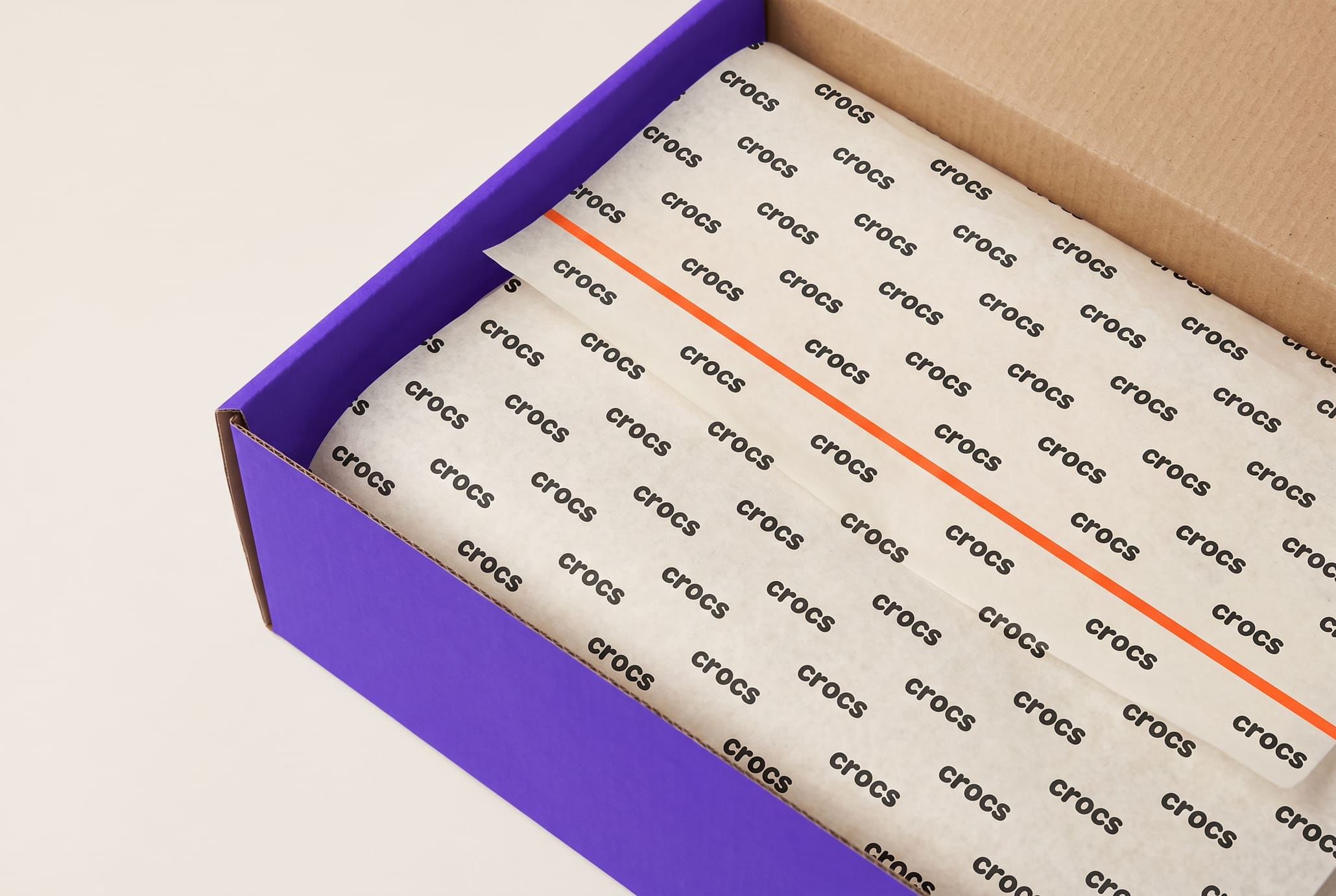 Cream tissue printed with a repeated CROCS wordmark inside an open ultraviolet shoebox.