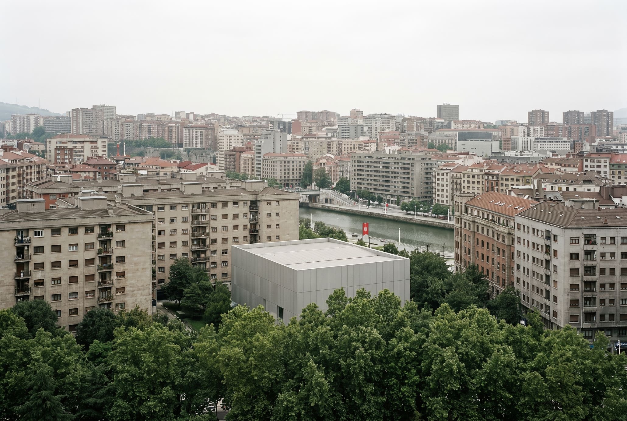 Overcast wide view of Bilbao with the low silver museum small and half hidden by trees