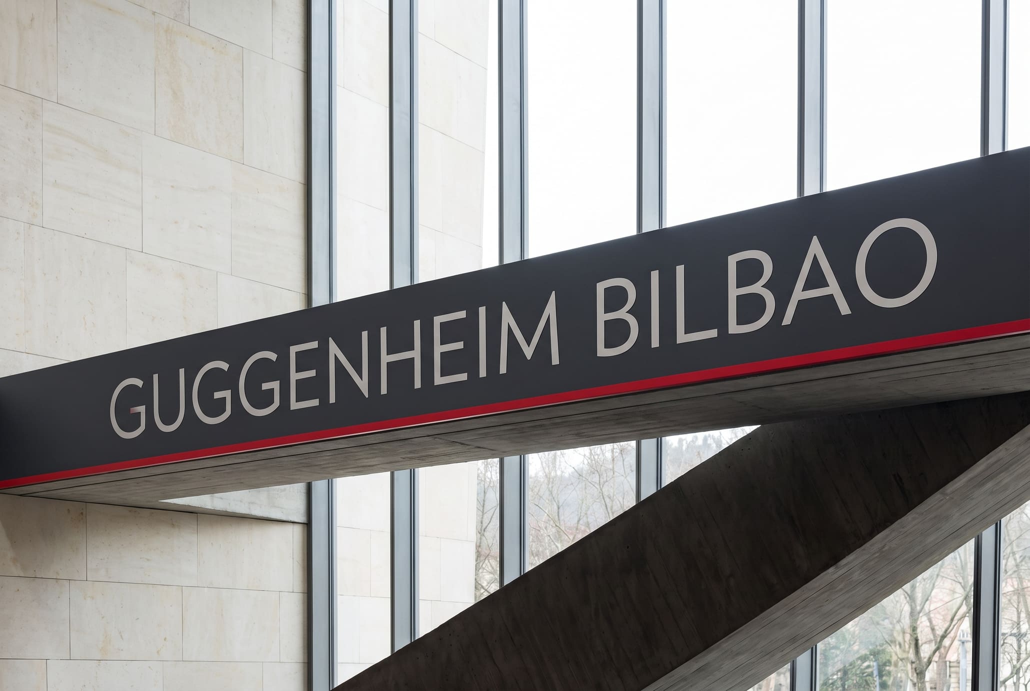 Slate band across limestone piers carrying GUGGENHEIM BILBAO in silver with a red hairline