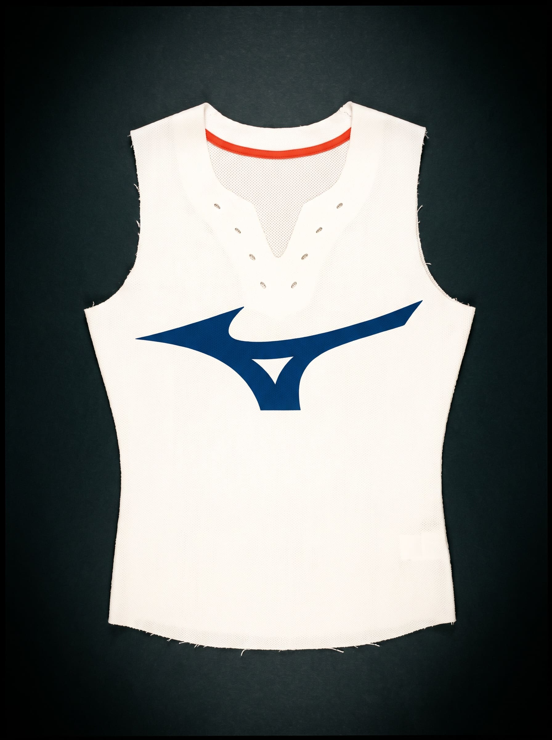 Flat-laid white running singlet with a large Mizuno-blue Runbird, raw-cut edges and a vermilion neck tape, on near-black.