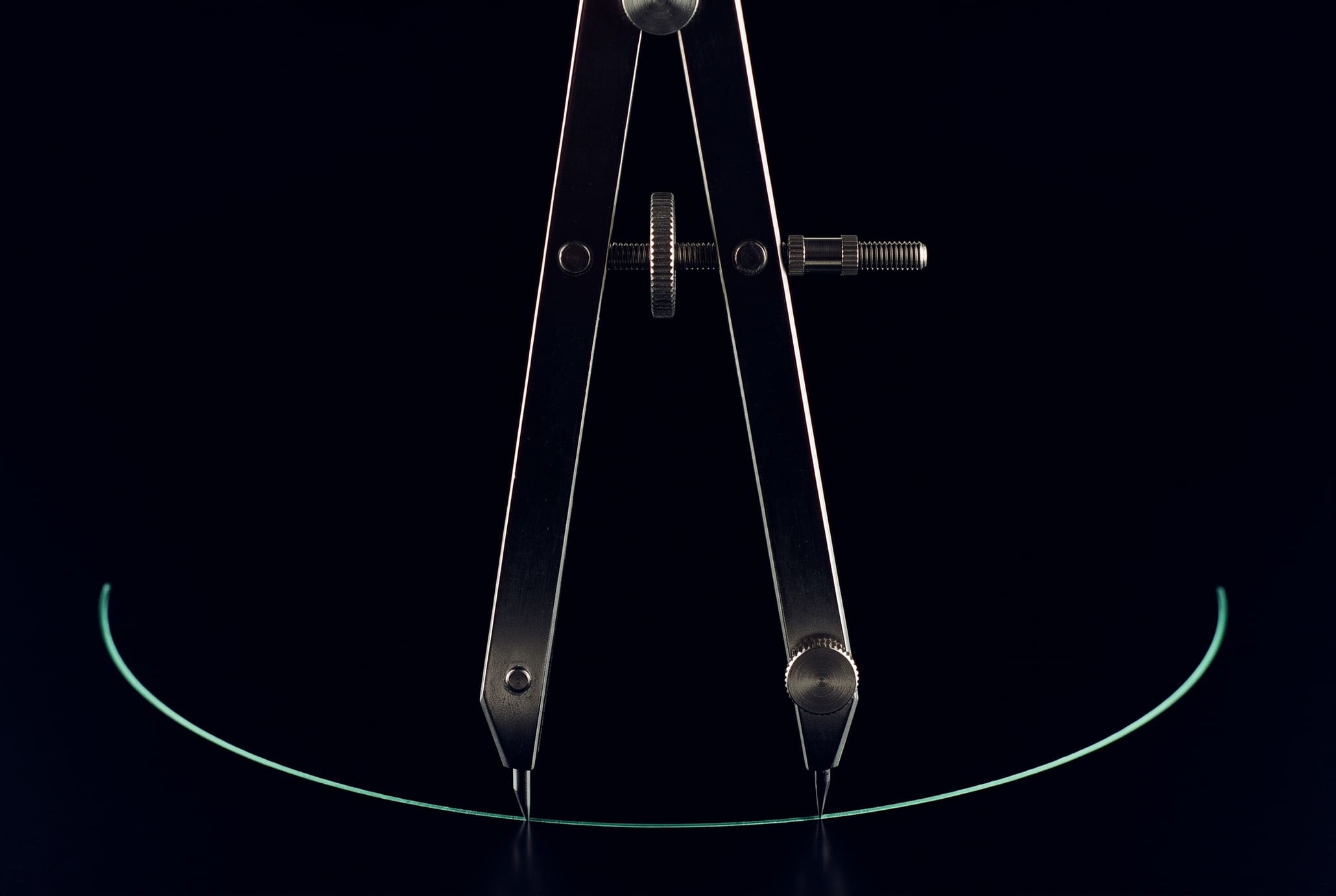 A steel drafting compass standing upright on pure black, lit only by thin specular highlights, with a single hairline mint arc scribed beneath its pen point
