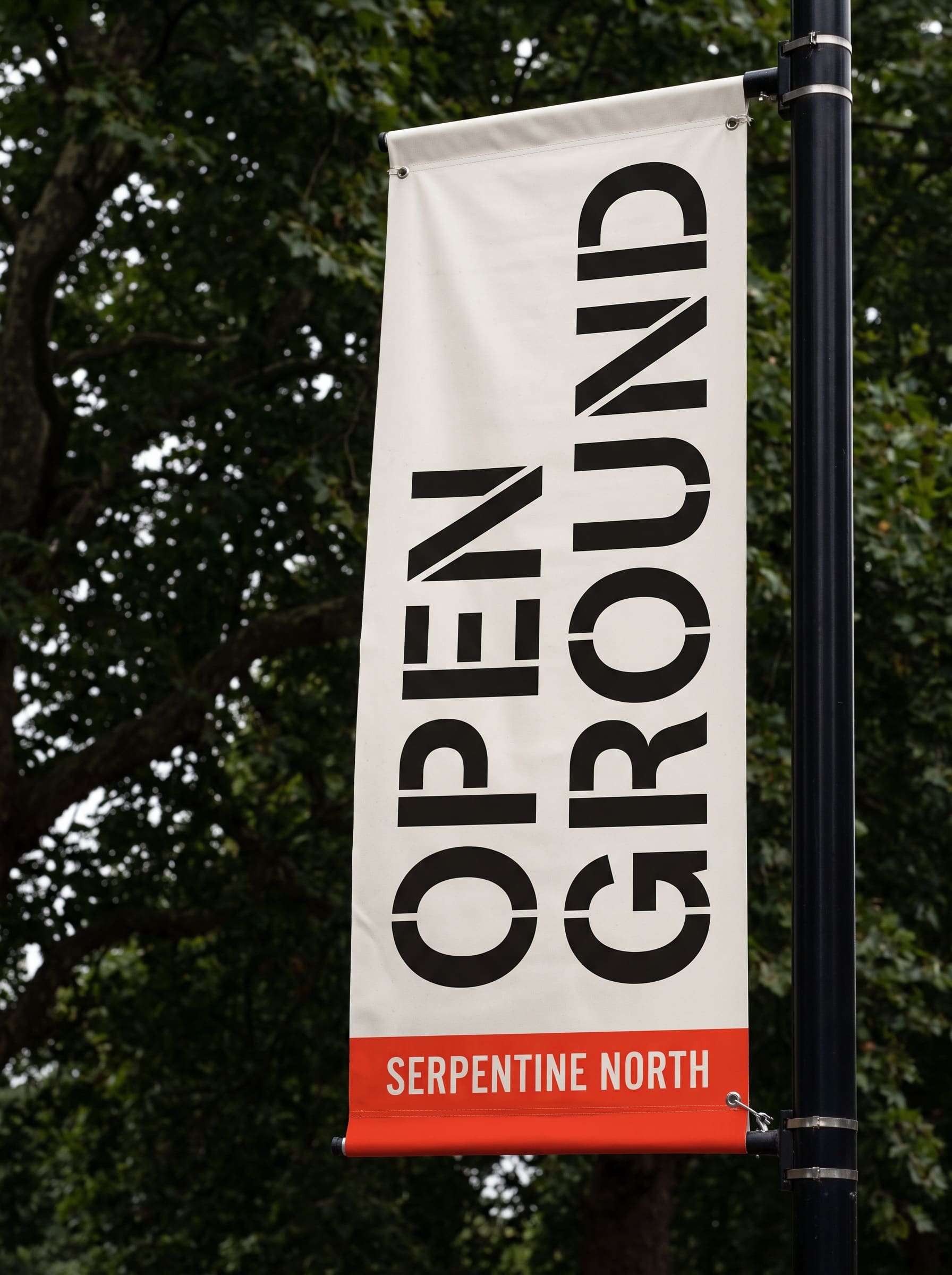 Off-white lamp-post banner reading OPEN GROUND above a red footer bar