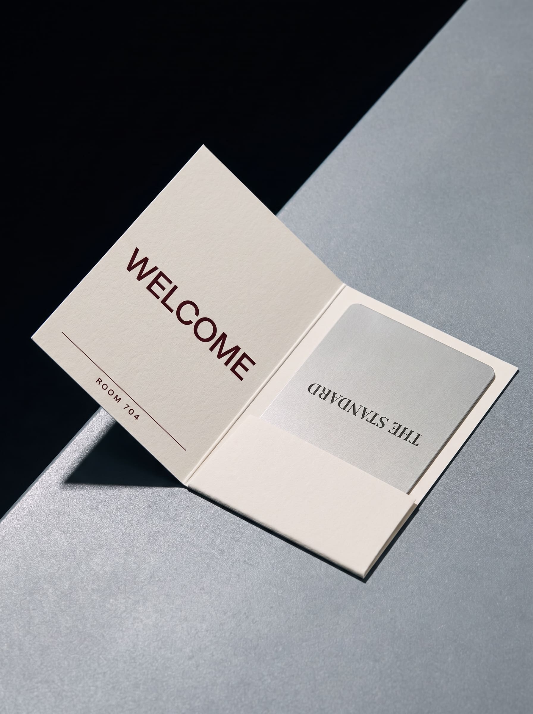 An opened cream keycard wallet printed WELCOME in oxblood, holding a chrome card with an upside-down wordmark.